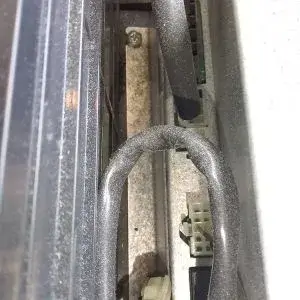 Dusty internal components of fitness equipment, showing cables, a screw, and a white connector within a narrow opening