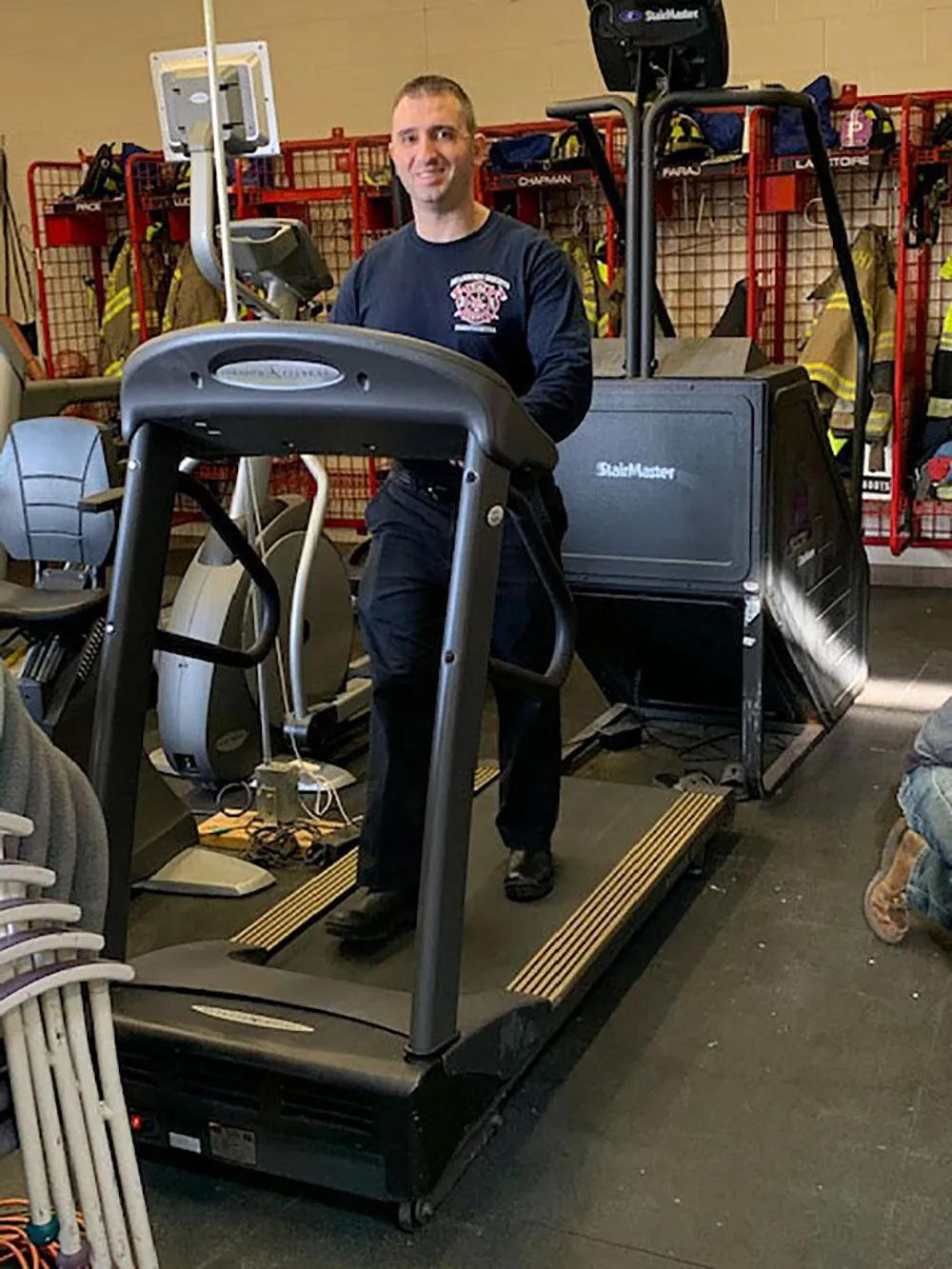 A smiling firefighter standing on a treadmill in a gym setting