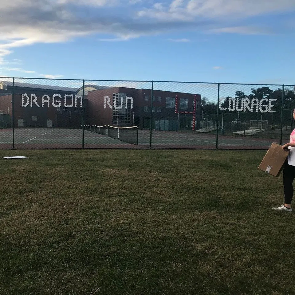 A school building and tennis courts seen beyond a fence